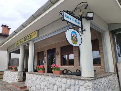 L'ingresso della pizzeria con l'insegna Ristoro alla Ruota, le colonne bianche, i gerani e i tavoli in veranda