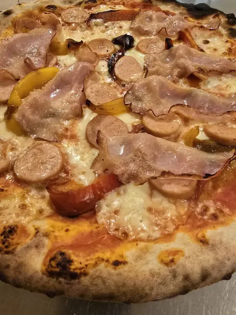 Primo piano della pizza Stuzzicante con pancetta affumicata, würstel e peperoni