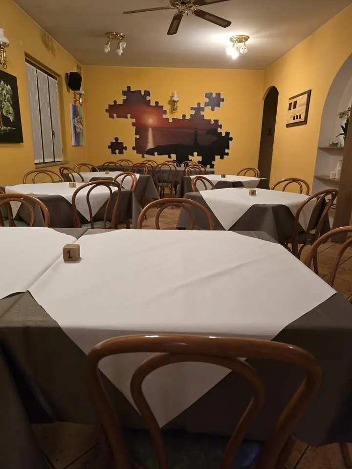 La sala della pizzeria con le pareti gialle, i tavoli apparecchiati e il grande murale a puzzle con il tramonto